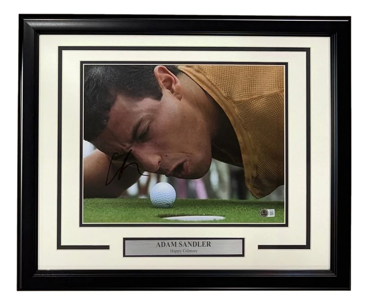 Adam Sandler signed 16x20 Happy Gilmore photo, lying on the green blowing at a golf ball beside the cup, with a Beckett hologram on the photo, in a black frame with white and black matting and a nameplate