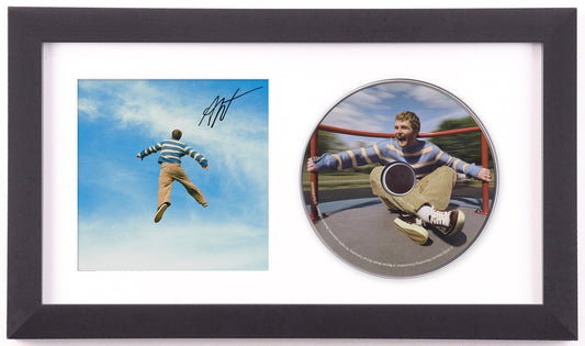 Alex Warren signed WILDCHILD framed CD display: signed art card of Warren flying against a blue sky, beside the album disc printed with him on a merry-go-round, in a white mat and black frame