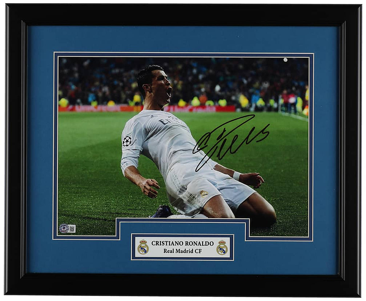 Cristiano Ronaldo signed 16x20 photo of his knee slide celebration in the white Real Madrid kit, with a Beckett hologram on the photo, in a black frame with blue matting and a Real Madrid nameplate