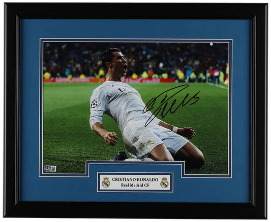Cristiano Ronaldo signed 16x20 photo of his knee slide celebration in the white Real Madrid kit, with a Beckett hologram on the photo, in a black frame with blue matting and a Real Madrid nameplate