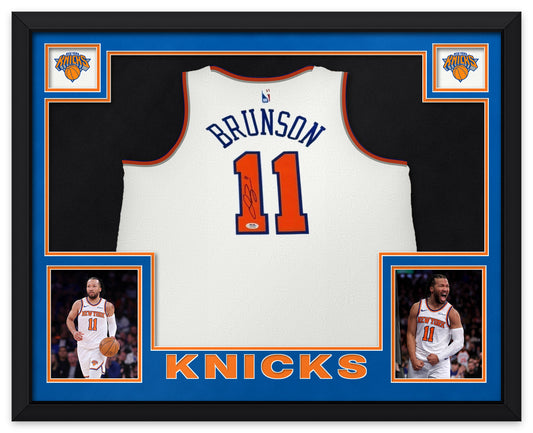 Jalen Brunson signed white New York Knicks number 11 jersey with the PSA sticker, shown in a black custom frame with blue and orange matting, Knicks logos in the upper corners, two photographs and KNICKS lettering