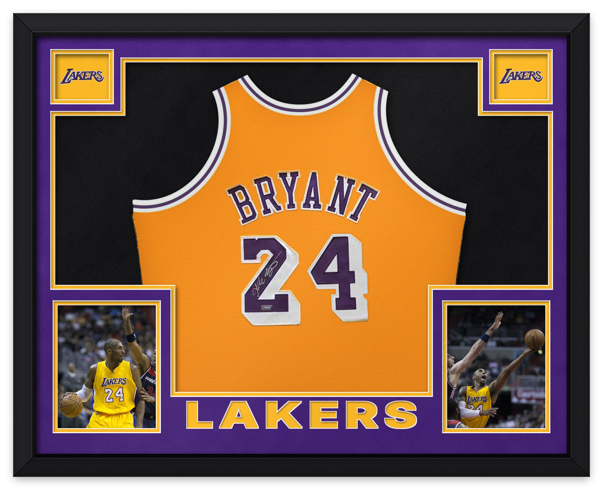 Kobe Bryant signed gold Los Angeles Lakers number 24 Mitchell and Ness jersey, signed in silver ink with the Panini Authentic hologram, shown in a black custom frame with purple and gold matting, Lakers wordmarks in the upper corners, two photographs and LAKERS lettering
