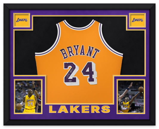 Kobe Bryant signed gold Los Angeles Lakers number 24 Mitchell and Ness jersey, signed in silver ink with the Panini Authentic hologram, shown in a black custom frame with purple and gold matting, Lakers wordmarks in the upper corners, two photographs and LAKERS lettering