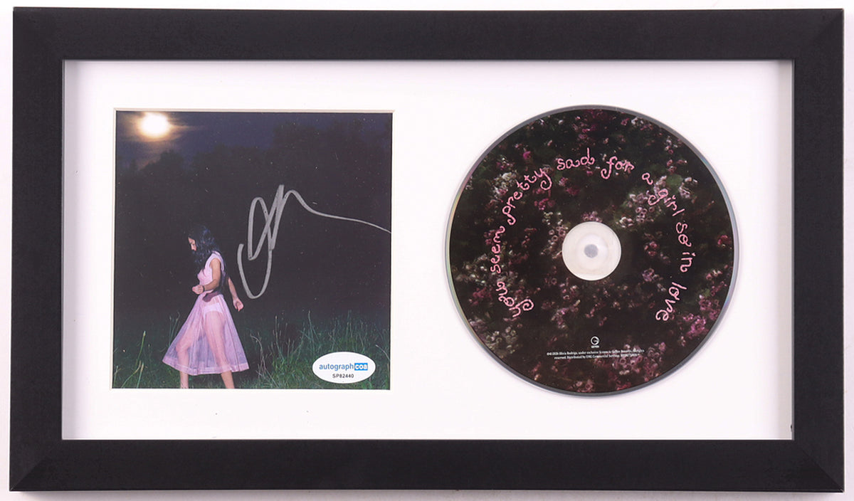 Olivia Rodrigo signed you seem pretty sad for a girl so in love framed CD display: night photo of Rodrigo in a sheer pink dress in tall grass under a full moon, signed in silver marker, ACOA label on the lower right, beside the floral album disc in a white mat and black frame