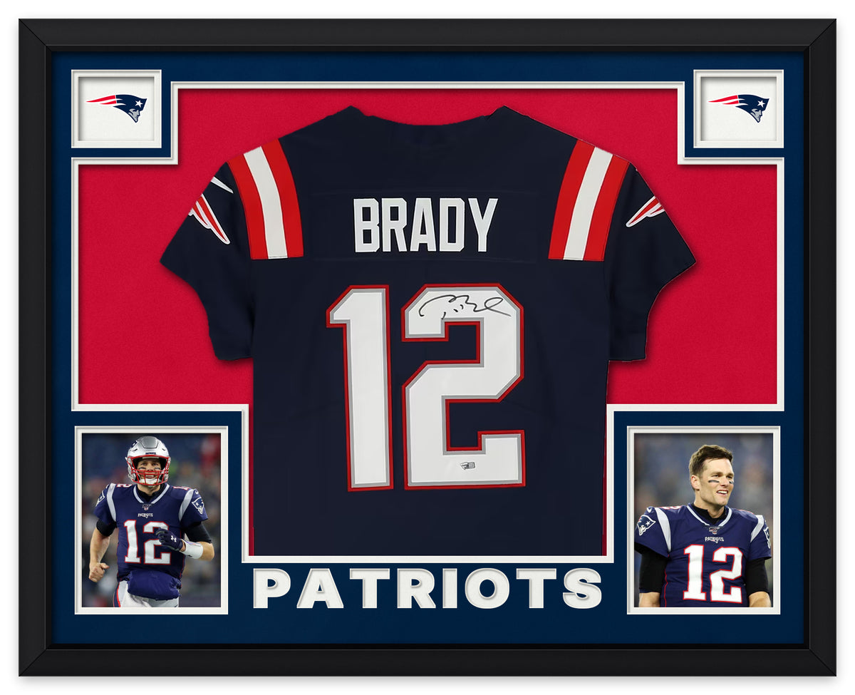 Tom Brady signed navy New England Patriots number 12 jersey in a black frame with navy matting, red backing, Patriots logos, two photos of Brady and PATRIOTS lettering